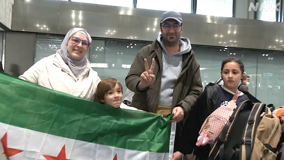 Aya Idrees, istri Mohammed (kiri), membentangkan bendera baru Suriah di bandara saat keluarganya bertolak dari Jepang pada akhir Maret.