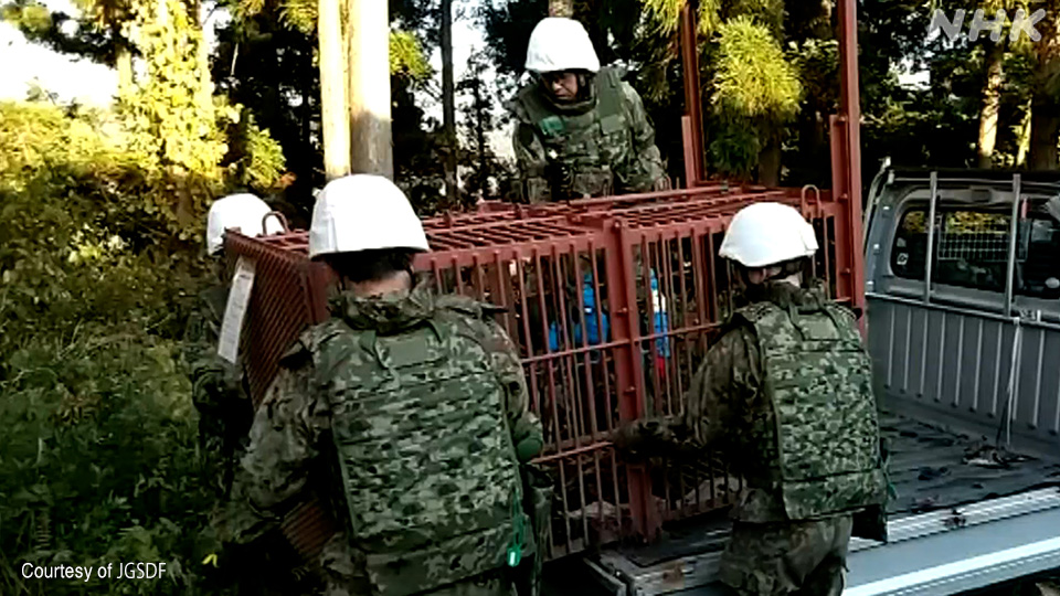 Personel Pasukan Bela Diri Darat membantu mengangkut jebakan kotak.