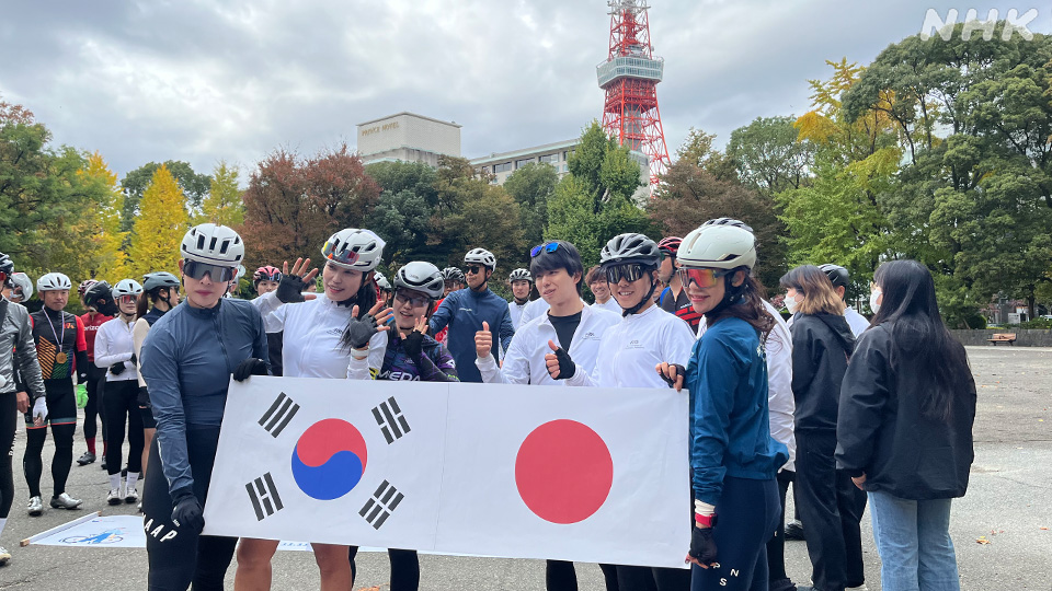 Para pesepeda berpose sambil memegang bendera Jepang dan Korea Selatan.