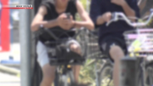 Seorang pesepeda di Jepang sedang berkendara di jalan raya sesuai dengan rambu-rambu lalu lintas.