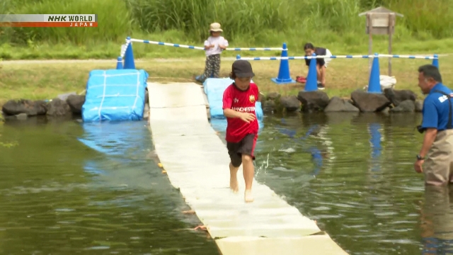 Anak-anak berlari menyeberangi kolam di atas tikar jerami apung di taman Mt. Fuji Children's World, Shizuoka